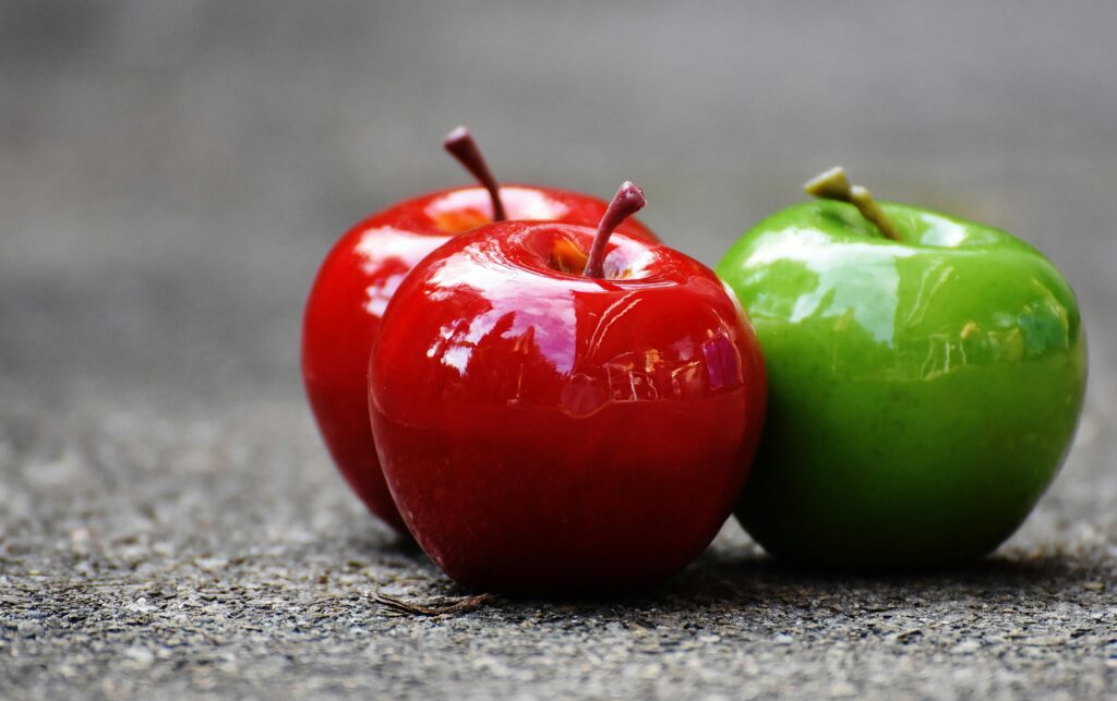 Close-up of shiny red and green apples on a textured surface, showcasing freshness and vibrant colors.